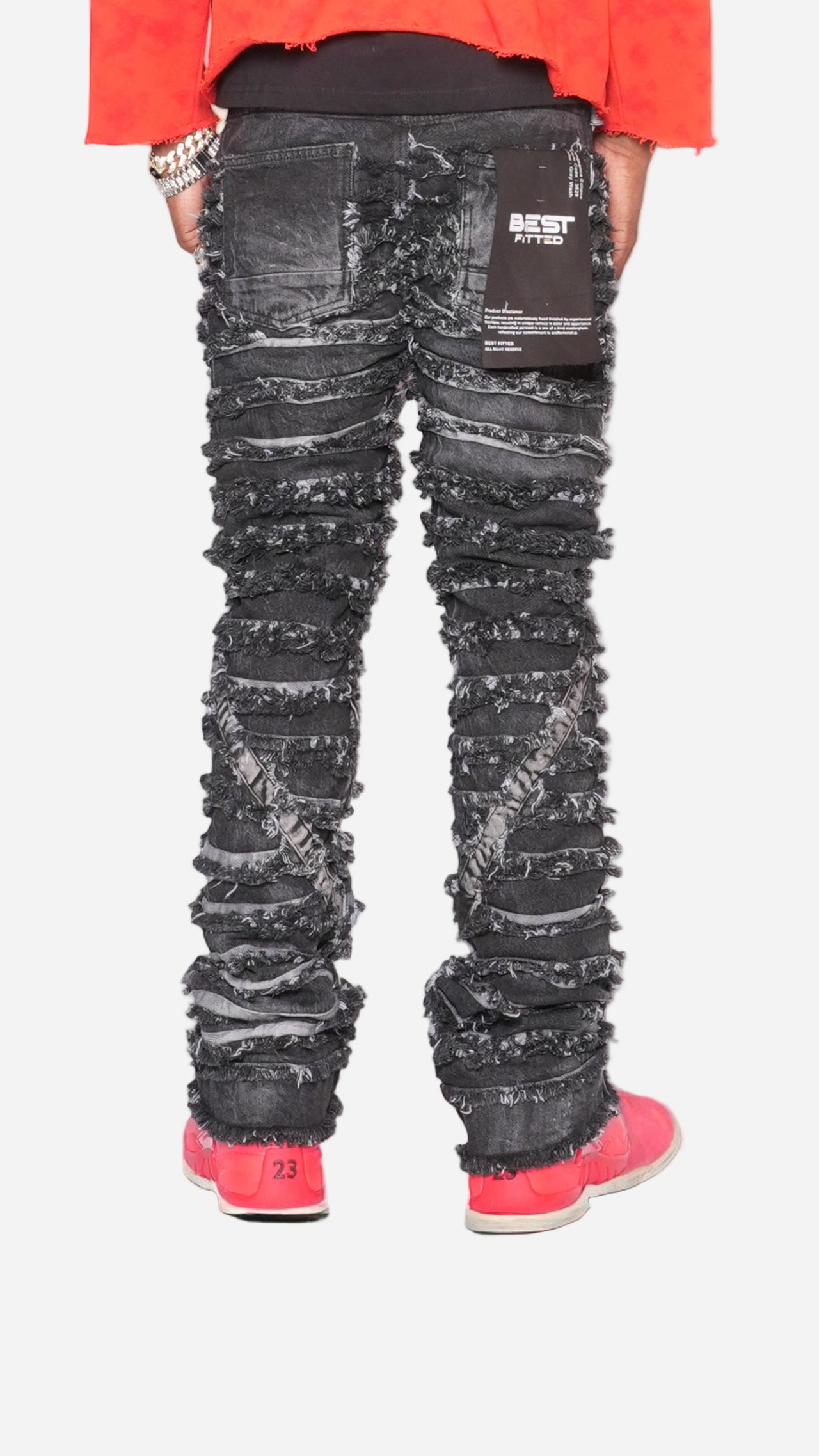 Person wearing black distressed jeans with a red jacket and pink shoes on a reflective surface.