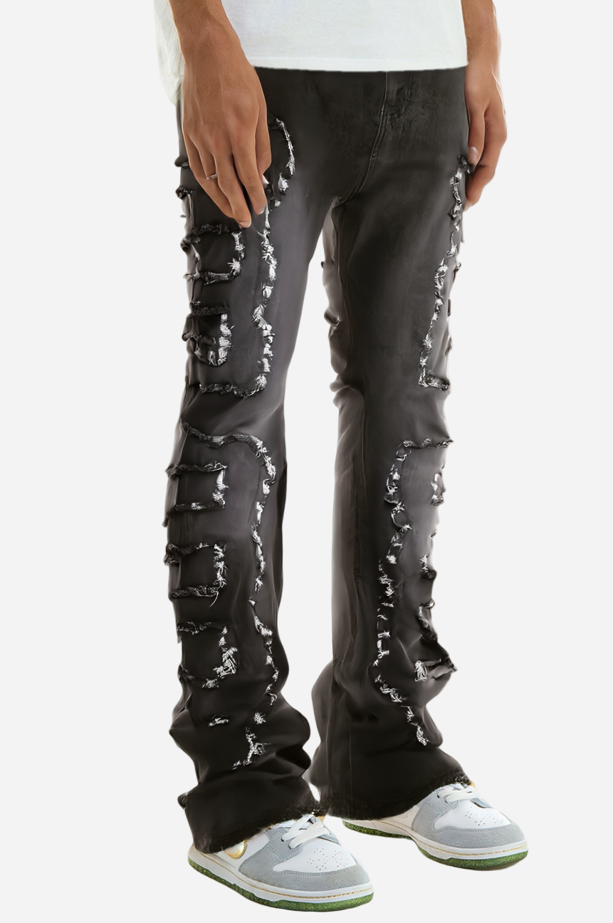 Black distressed jeans with white paint splashes worn by a person on a white background